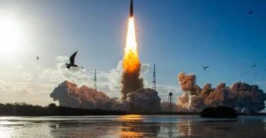 Photographie du décollage de la fusée SLS de la NASA depuis le Kennedy Space Center pour la mission Artemis II, montrant une colonne de feu intense et de la fumée s'élevant au-dessus d'un plan d'eau avec des oiseaux en vol au premier plan.