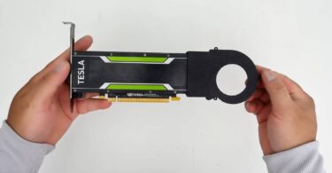Vue de dessus d'une carte graphique Nvidia Tesla low-profile, modifiée avec un carénage de ventilateur passif noir imprimé en 3D, tenue en main par une personne portant un pull gris sur un fond blanc.