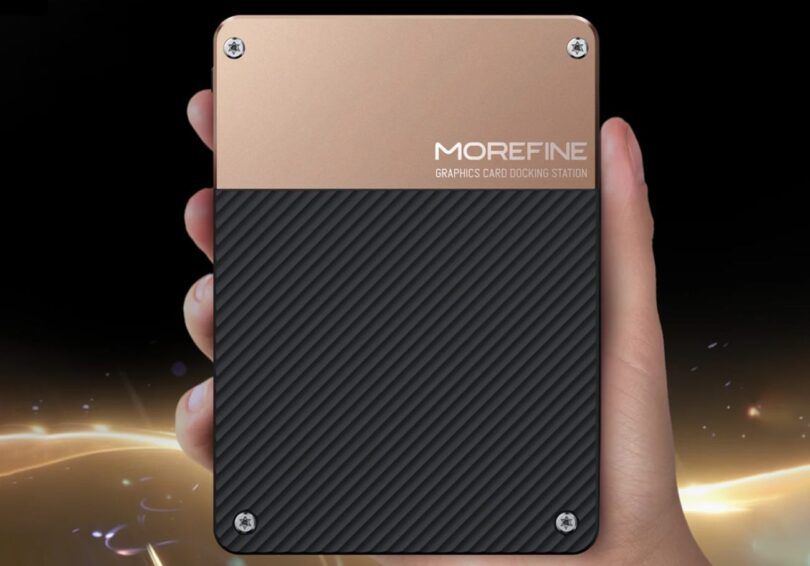 Vue de dessus du boîtier eGPU Morefine G2 tenu dans une main, illustrant sa taille ultra-compacte. Le châssis présente une finition bicolore or brossé et noir strié avec le logo Morefine Graphics Card Docking Station.