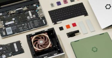 Vue en plongée d'un ordinateur portable Framework ouvert montrant sa batterie, ses modules de mémoire et son ventilateur, entouré de composants interchangeables comme un clavier, des ports USB-C colorés et une coque verte.