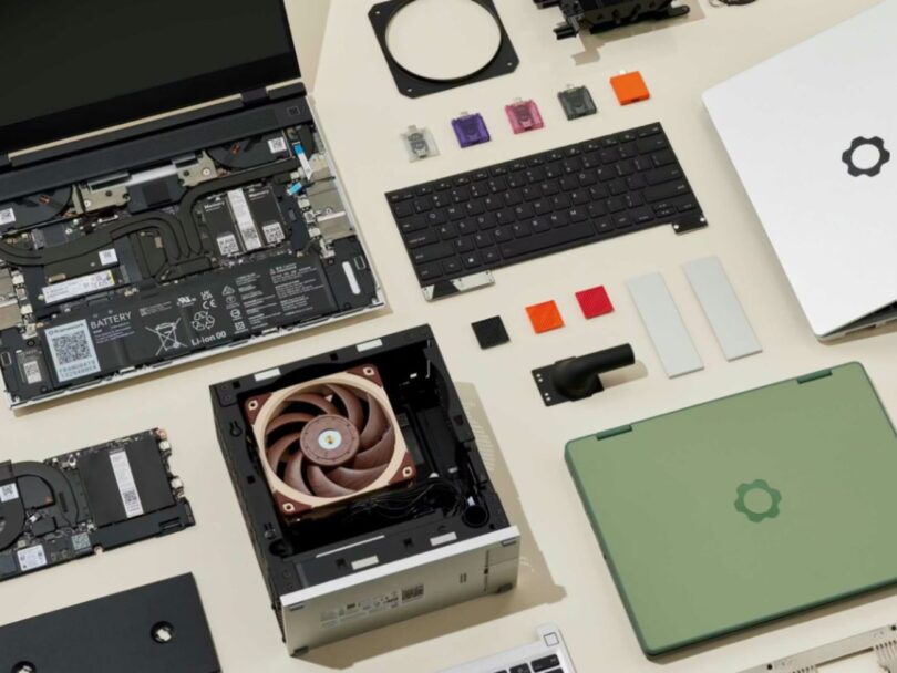 Vue en plongée d'un ordinateur portable Framework ouvert montrant sa batterie, ses modules de mémoire et son ventilateur, entouré de composants interchangeables comme un clavier, des ports USB-C colorés et une coque verte.