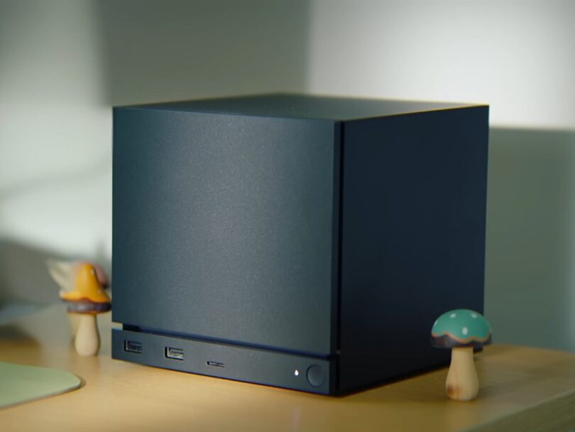 Image conceptuelle générée par IA d'un mini-PC Valve compact et élégant, positionné sur un bureau en bois. L'appareil est un cube noir mat aux lignes épurées, illustrant l'esthétique possible de la nouvelle console de salon de l'entreprise.