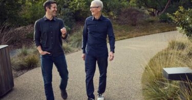 John Ternus et Tim Cook marchant côte à côte et discutant sur le campus de l'Apple Park, illustrant la transition de leadership chez Apple en 2026.