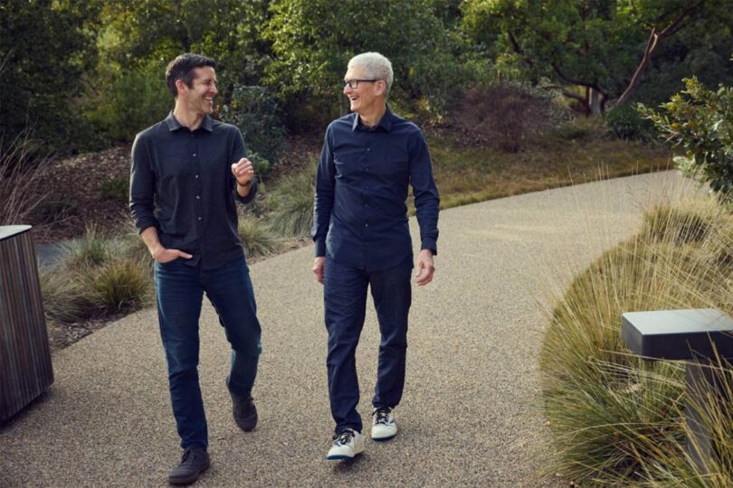 John Ternus et Tim Cook marchant côte à côte et discutant sur le campus de l'Apple Park, illustrant la transition de leadership chez Apple en 2026.