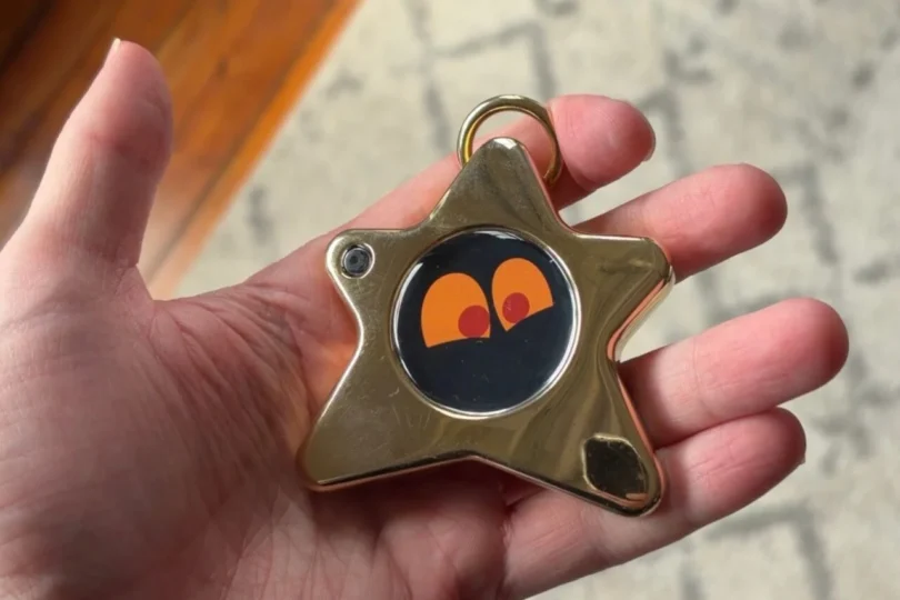 Gros plan sur le Starboy, un porte-clés connecté en forme d'étoile dorée avec un écran OLED affichant des yeux expressifs orange, tenu dans une main.