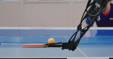 Gros plan d'un bras robotique Sony équipé d'une raquette de tennis de table, s'apprêtant à frapper une balle orange avec une précision millimétrée sur une table officielle.