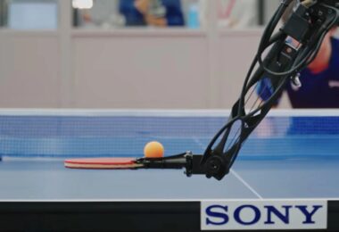 Gros plan d'un bras robotique Sony équipé d'une raquette de tennis de table, s'apprêtant à frapper une balle orange avec une précision millimétrée sur une table officielle.