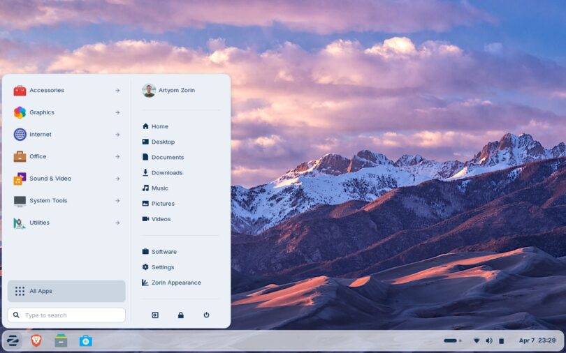 Capture d'écran du bureau Zorin OS 18.1 montrant le menu "Zorin" ouvert avec les catégories d'applications, le dossier utilisateur et un fond d'écran de montagnes enneigées au coucher du soleil.