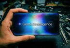 Smartphone tenu en main affichant le logo Gemini Intelligence de Google sur un fond étoilé et lumineux, posé sur un plan de travail électronique en vue de l'intégration dans Android 17.
