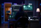 Illustration cybersécurité représentant un attaquant encapuchonné face à trois écrans affichant du code d'exploit et des visualisations d'intrusion, scène typique d'exploitation d'une vulnérabilité Windows comme la faille BitLocker YellowKey CVE-2026-45585.