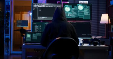 Illustration cybersécurité représentant un attaquant encapuchonné face à trois écrans affichant du code d'exploit et des visualisations d'intrusion, scène typique d'exploitation d'une vulnérabilité Windows comme la faille BitLocker YellowKey CVE-2026-45585.