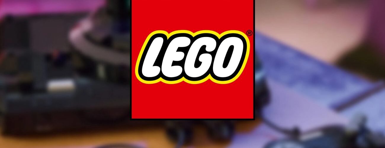 Logo officiel LEGO superposé en premier plan sur un arrière-plan flou montrant une console de jeux rétro noire avec ses manettes filaires sur une table en bois.