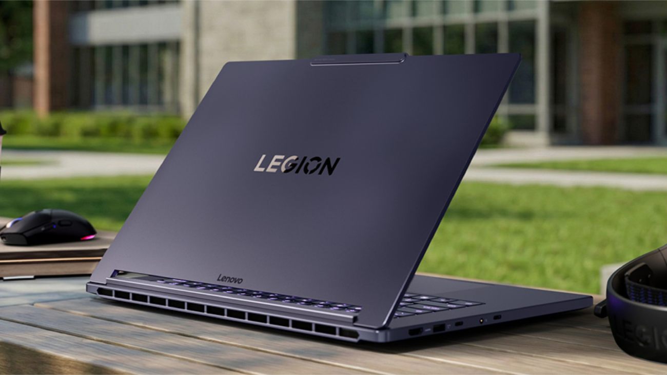 Vue arrière du laptop Lenovo Legion 7a 15ASH11 dans sa finition violette distinctive, posé sur une table en bois à l'extérieur. Le logo Legion est centré sur le capot, révélant les larges grilles de ventilation à la base de l'écran OLED.