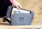 Visuel conceptuel d'une Nintendo Switch 2 insérée dans sa station d'accueil grise affichant le logo "Switch 2", illustrant l'annonce de la hausse de prix de 10 000 yens au Japon.