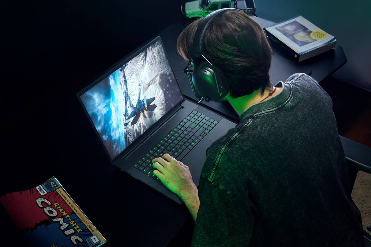 Vue en plongée d'un joueur équipé d'un casque audio utilisant le PC portable Razer Blade 18 2026, affichant un jeu vidéo de simulation de vol spatial sur son grand écran de 18 pouces.