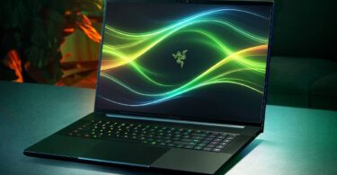 Ordinateur portable gaming Razer Blade 18 modèle 2026 ouvert sur une table, affichant un fond d'écran abstrait vert et le logo de la marque, avec son clavier rétroéclairé RGB actif.
