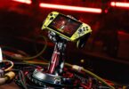 Console Asus ROG Xbox Ally X personnalisée aux couleurs de Cyberpunk 2077 (jaune vieilli), maintenue par un support exclusif en forme de bras cybernétique de Johnny Silverhand, entourée de câbles.