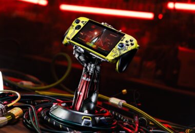 Console Asus ROG Xbox Ally X personnalisée aux couleurs de Cyberpunk 2077 (jaune vieilli), maintenue par un support exclusif en forme de bras cybernétique de Johnny Silverhand, entourée de câbles.
