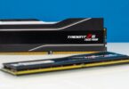Deux barrettes de mémoire vive G.Skill Trident Z5 RGB Neo DDR5 noires avec dissipateur thermique en aluminium brossé et diffuseur LED RGB, posées sur une surface blanche devant un fond bleu.