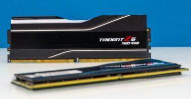 Deux barrettes de mémoire vive G.Skill Trident Z5 RGB Neo DDR5 noires avec dissipateur thermique en aluminium brossé et diffuseur LED RGB, posées sur une surface blanche devant un fond bleu.