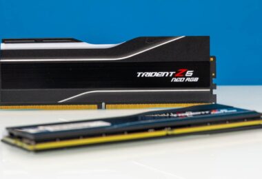Deux barrettes de mémoire vive G.Skill Trident Z5 RGB Neo DDR5 noires avec dissipateur thermique en aluminium brossé et diffuseur LED RGB, posées sur une surface blanche devant un fond bleu.
