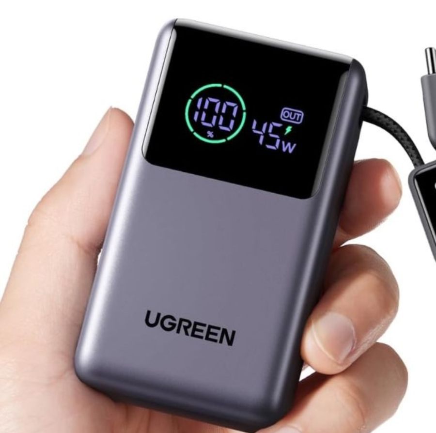 Main tenant une batterie externe compacte Ugreen grise avec écran LED affichant 100% de charge et une puissance de sortie de 45W via son câble USB-C intégré.