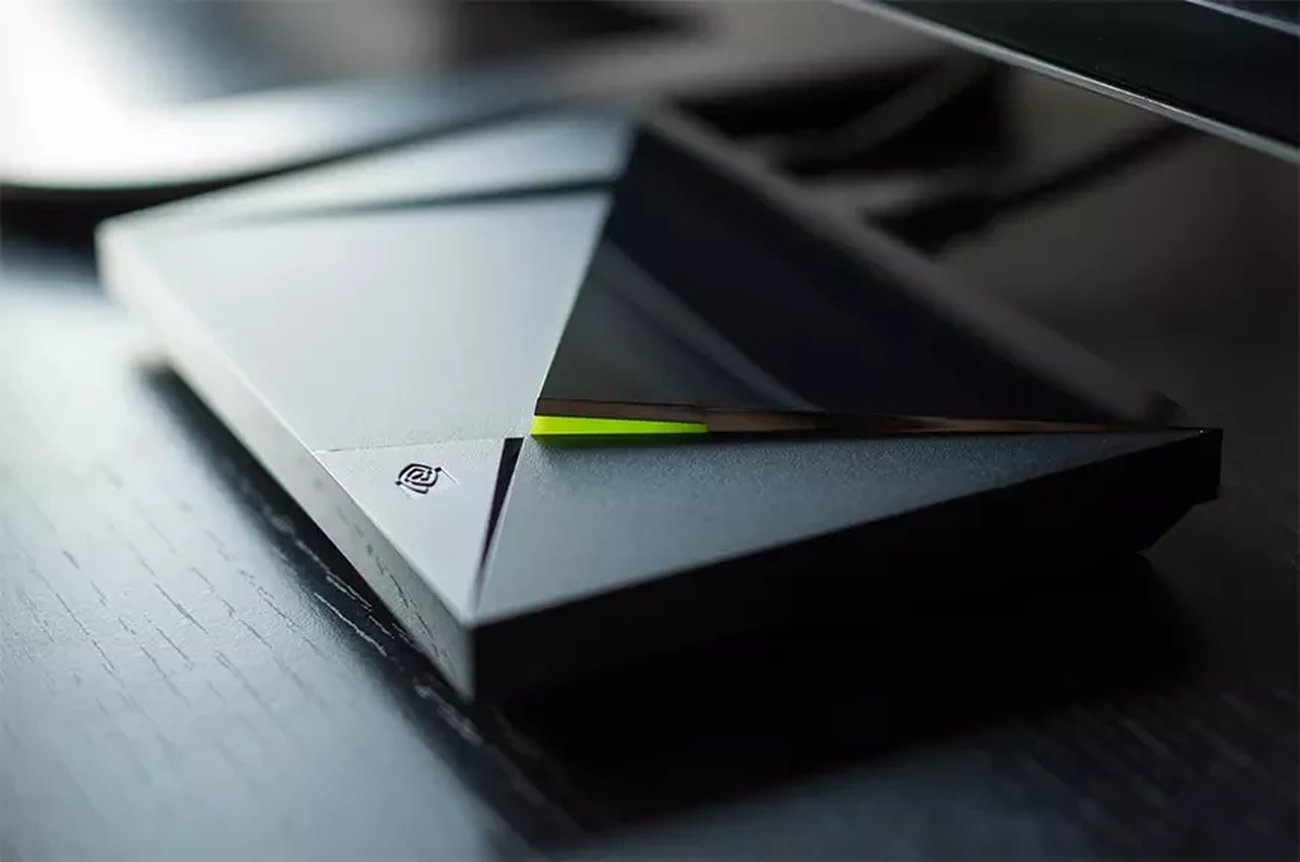 Gros plan sur le boîtier Nvidia Shield TV Pro posé sur un bureau en bois sombre, avec ses facettes triangulaires noires, le logo NVIDIA gravé et le liseré LED vert allumé.