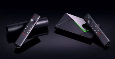Nvidia Shield TV Pro et Shield TV posées sur fond noir avec leurs télécommandes, la Pro et son liseré vert à droite, le modèle cylindrique à gauche, illustrant la hausse de prix de 2026.